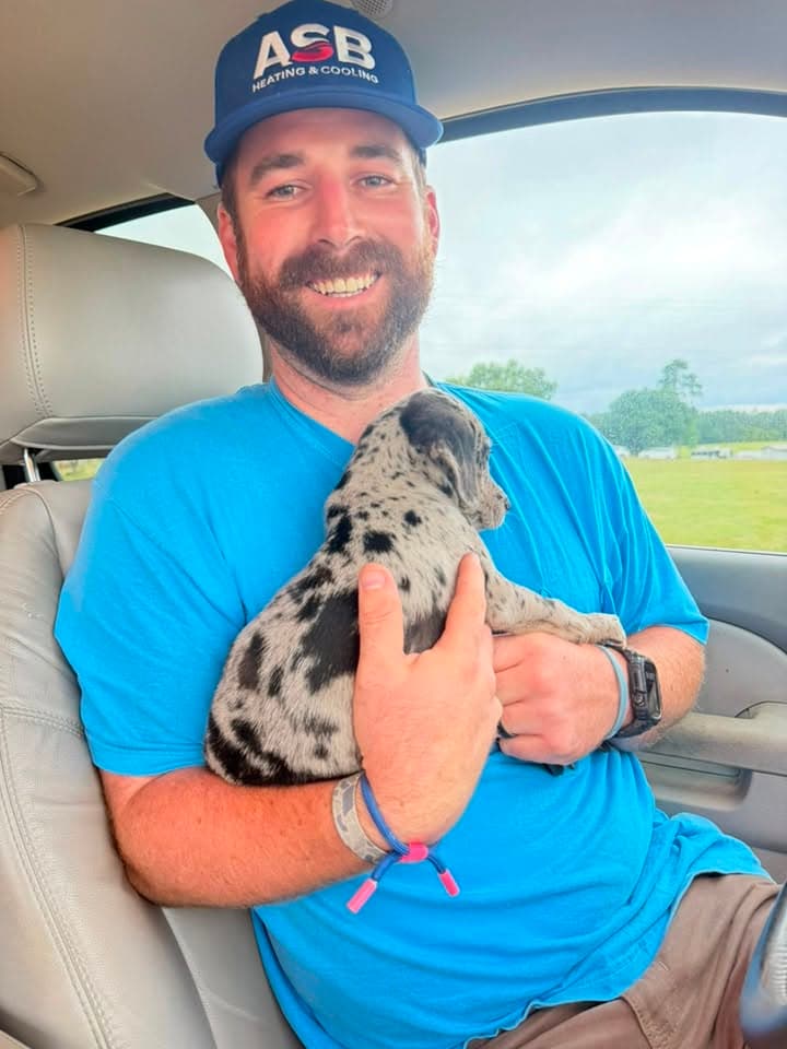 Troy Gregory smiling in his work truck, holding a spotted puppy